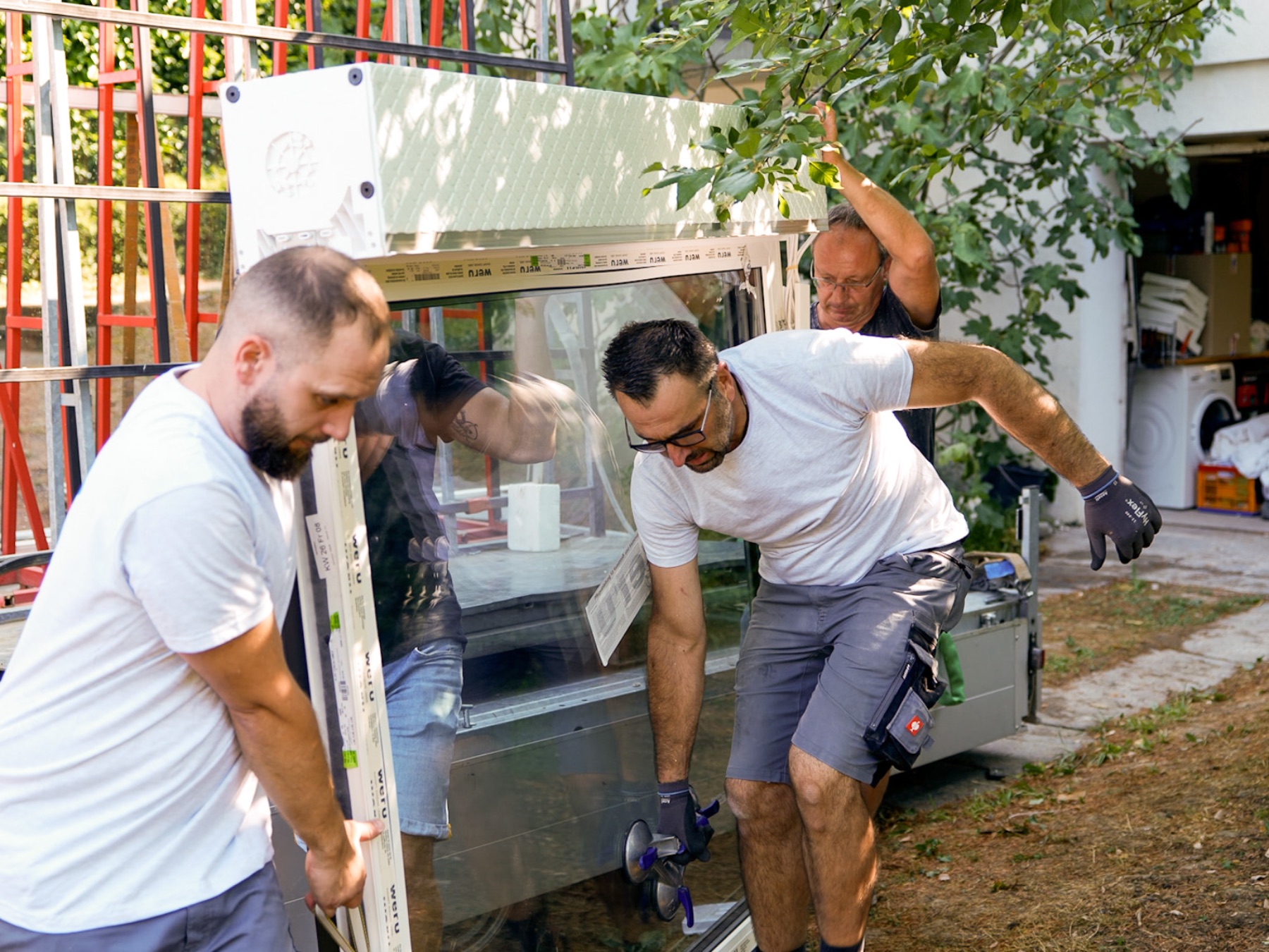 Zwei Monteure heben ein großes Fensterelement vom Anhänger