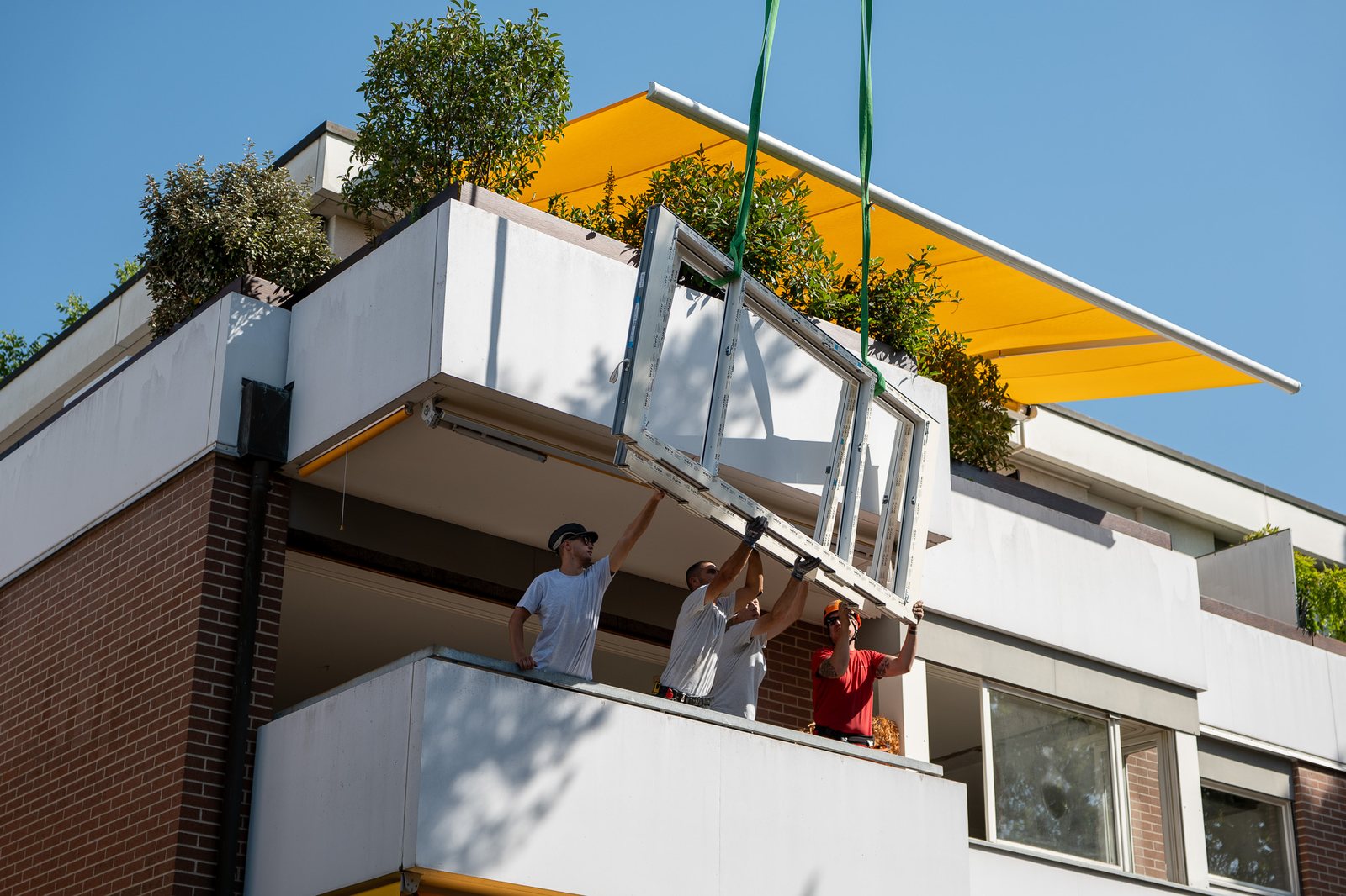 Monteure nehmen ein Fensterelement am Kran auf dem Balkon entgegen