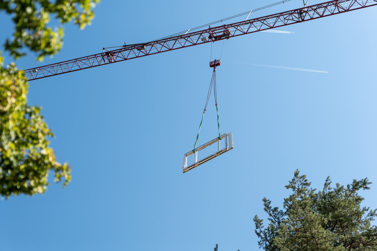 Fensterelement schwebt am Kranhaken vor blauem Himmel